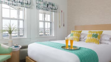 A hotel room with a bed, a bedside table with a lamp, a window with a view, and a plant.