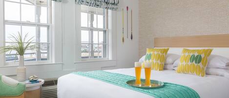 A hotel room with a bed, a bedside table with a lamp, a window with a view, and a plant.