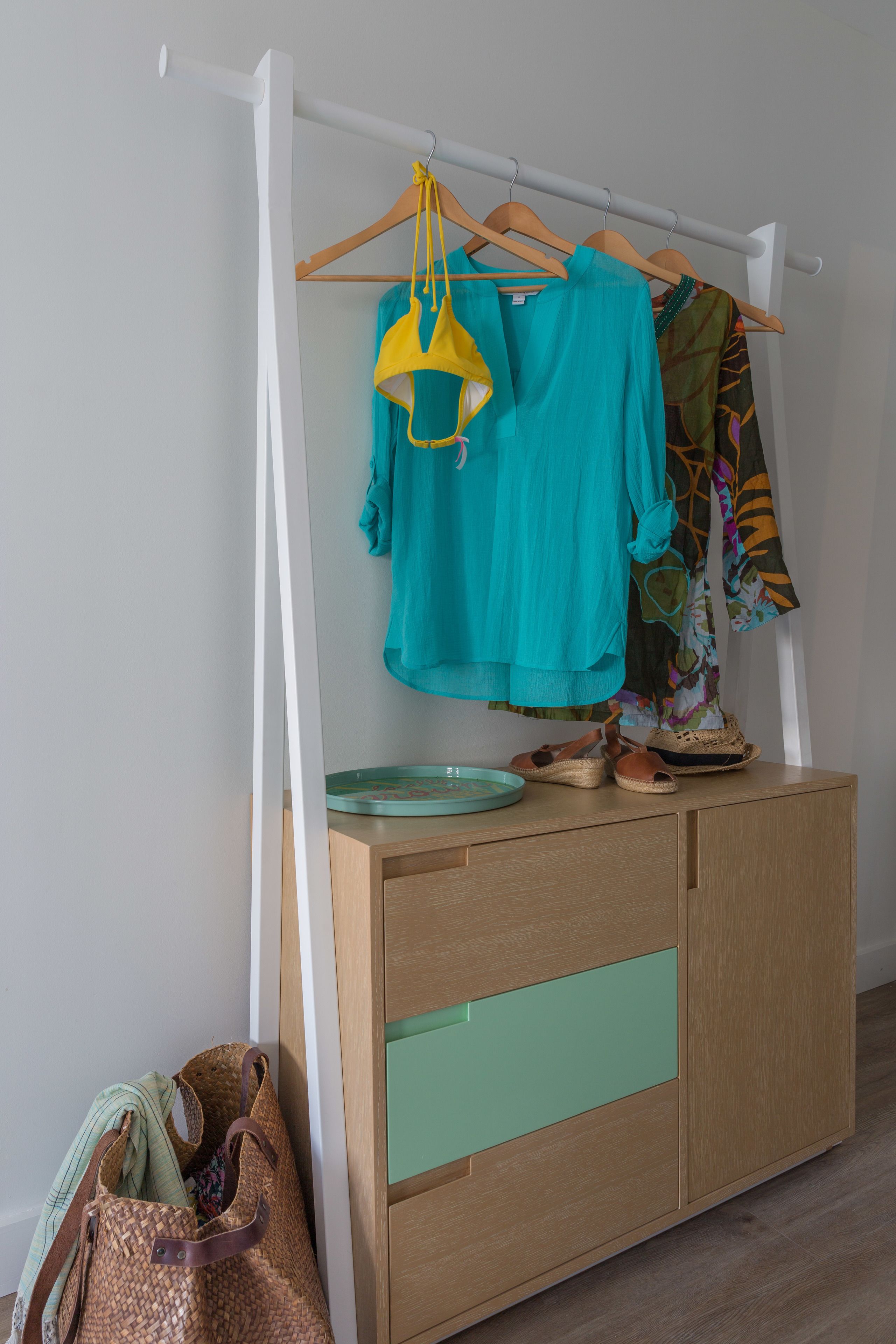 Un armario de madera con un cajón verde, una barra para colgar ropa y un bolso tejido.
