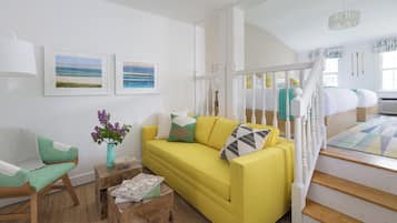 A bright yellow sofa with a white railing staircase, a wooden coffee table, and a framed picture of a beach.