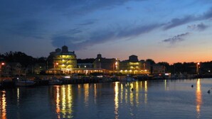 A waterfront hotel with a prominent building reflecting on the water, boats docked nearby, and a clear sky at dusk. - Summercamp (Oak Bluffs)