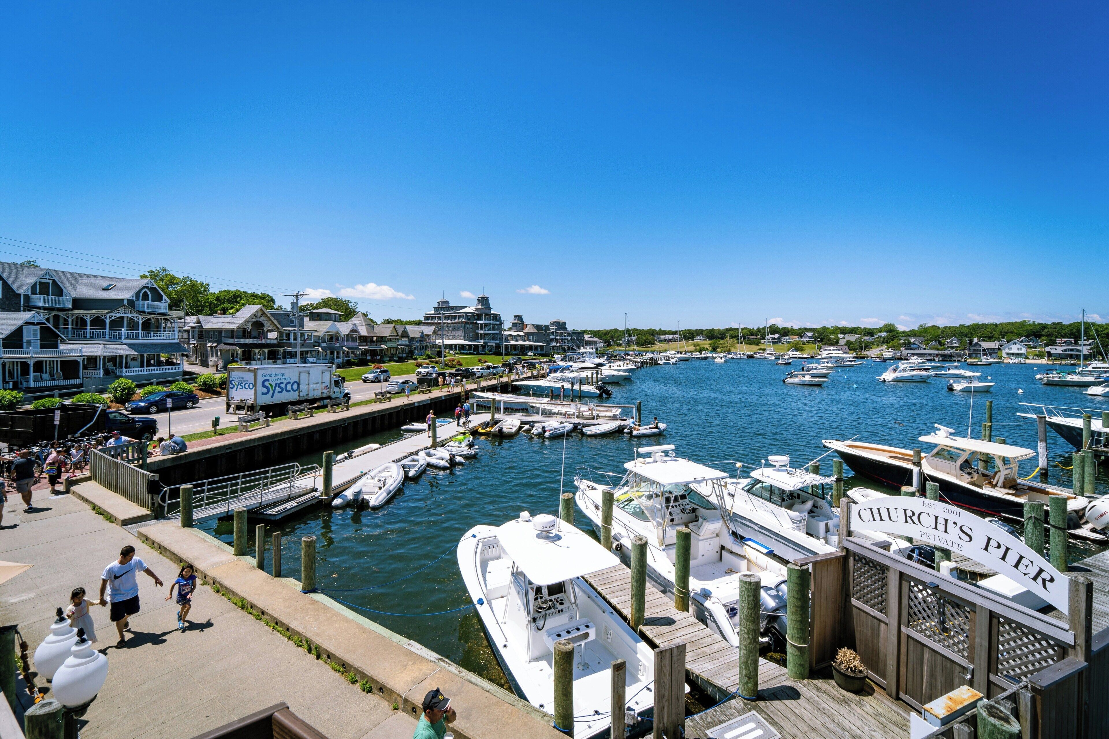 A marina with boats docked, a dockside walkway, and buildings in the background.