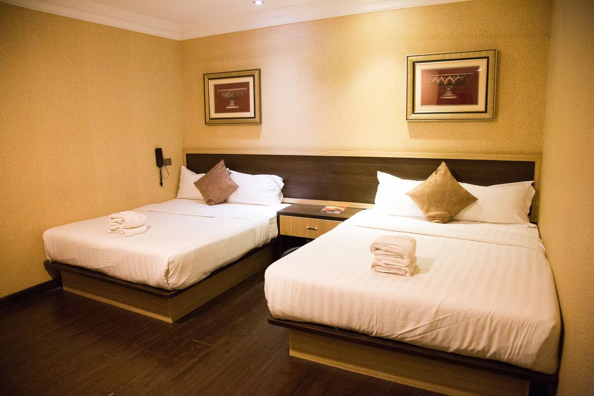 A hotel room with two beds, each with white linens and pillows, a wooden headboard, a nightstand, and a wall-mounted phone.
