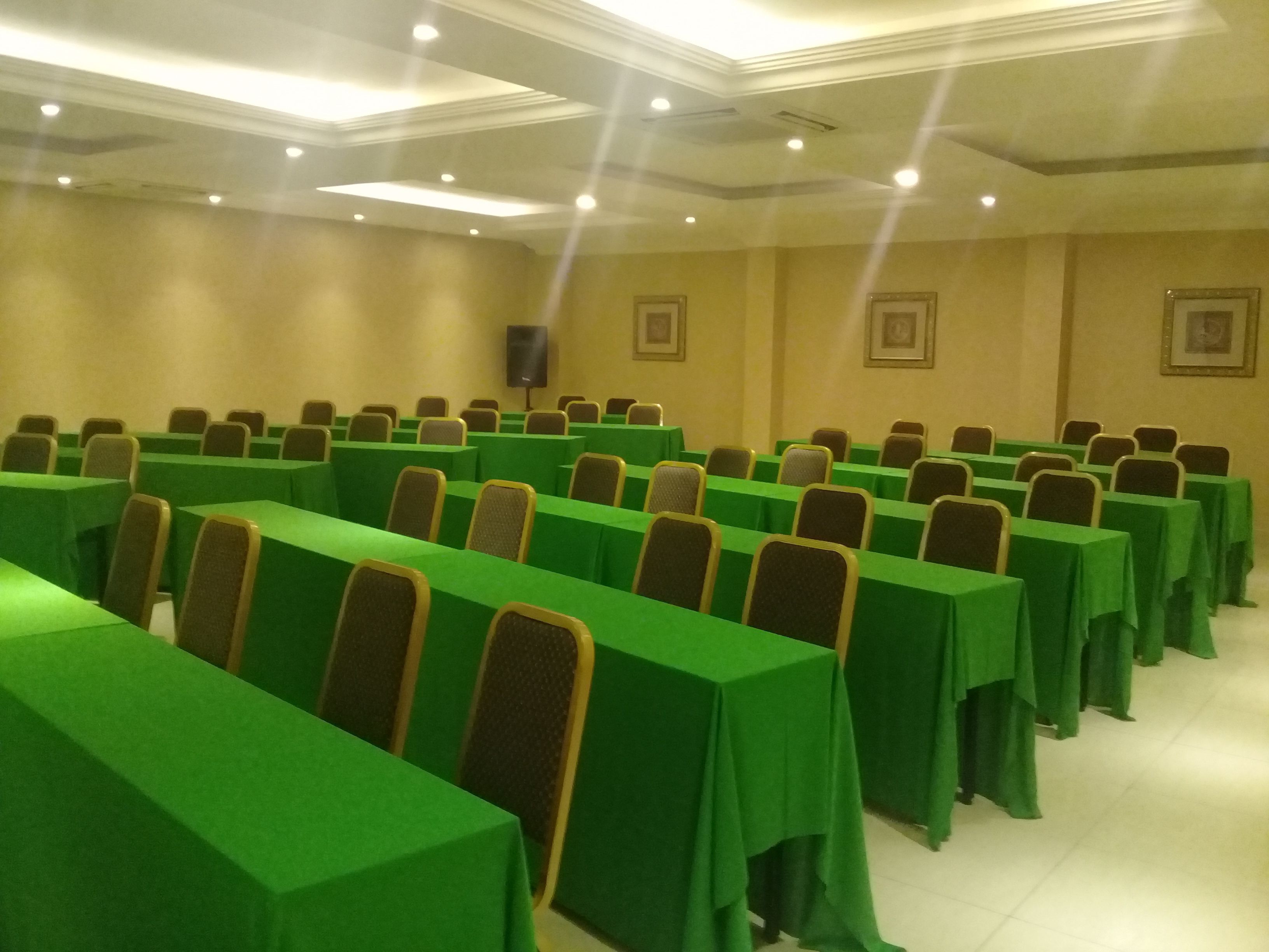 A conference room with rows of tables covered in green tablecloths and chairs with brown headrests.