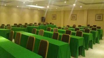 A conference room with rows of tables covered in green tablecloths and chairs with brown headrests.
