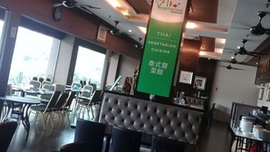 A restaurant interior with a green sign indicating Thai vegetarian cuisine, multiple tables and chairs, ceiling fans, and a large window providing natural light. - Valenza Hotel & Cafe (Kuala Lumpur)