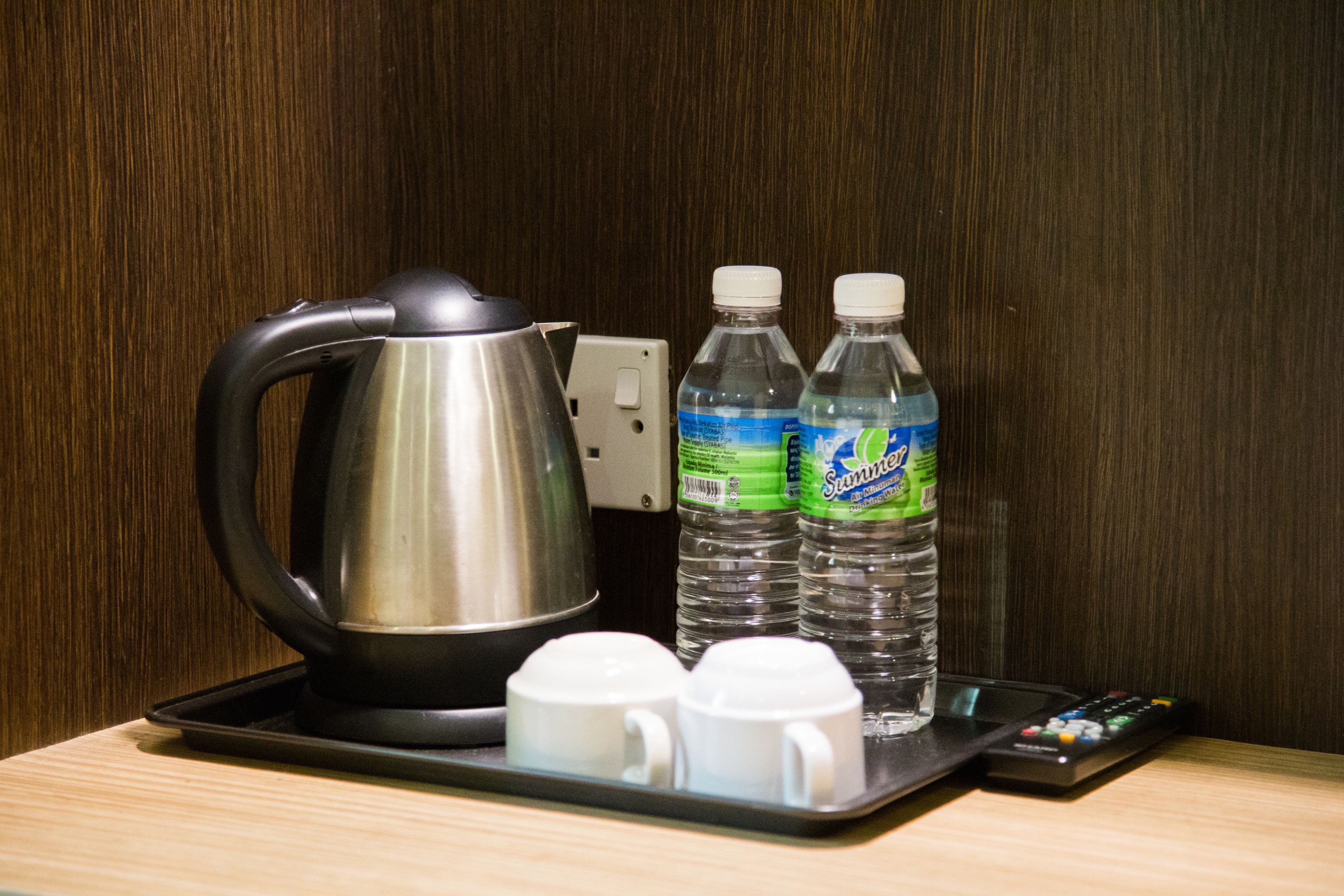 A tray with a kettle, two bottles of water, and two white mugs on a wooden surface.