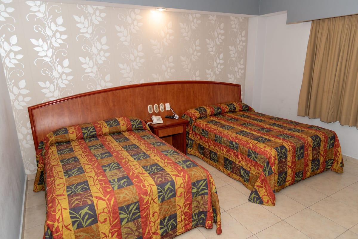 Une chambre d’hôtel avec deux lits simples, une tête de lit en bois, une table de chevet avec un téléphone et un papier peint à motifs floraux.