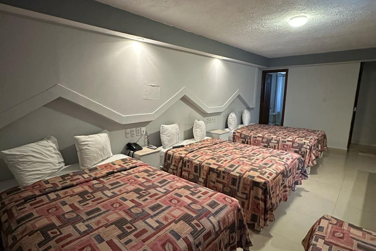 Une chambre d’hôtel avec quatre lits, chacun doté d’une literie à motifs, un petit bureau avec un téléphone et un luminaire fixé au mur.