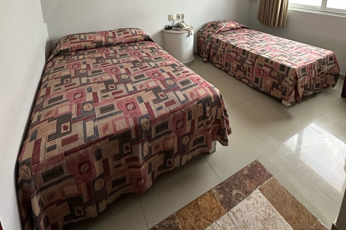 Une chambre avec deux lits, une petite table et une fenêtre avec des rideaux.