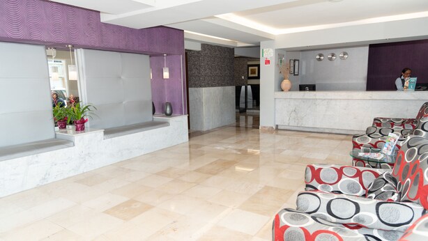 Et hotellets receptionområde med en skrivebord af marmor, et venteområde med mønstrede sofaer og en receptionsdisk.