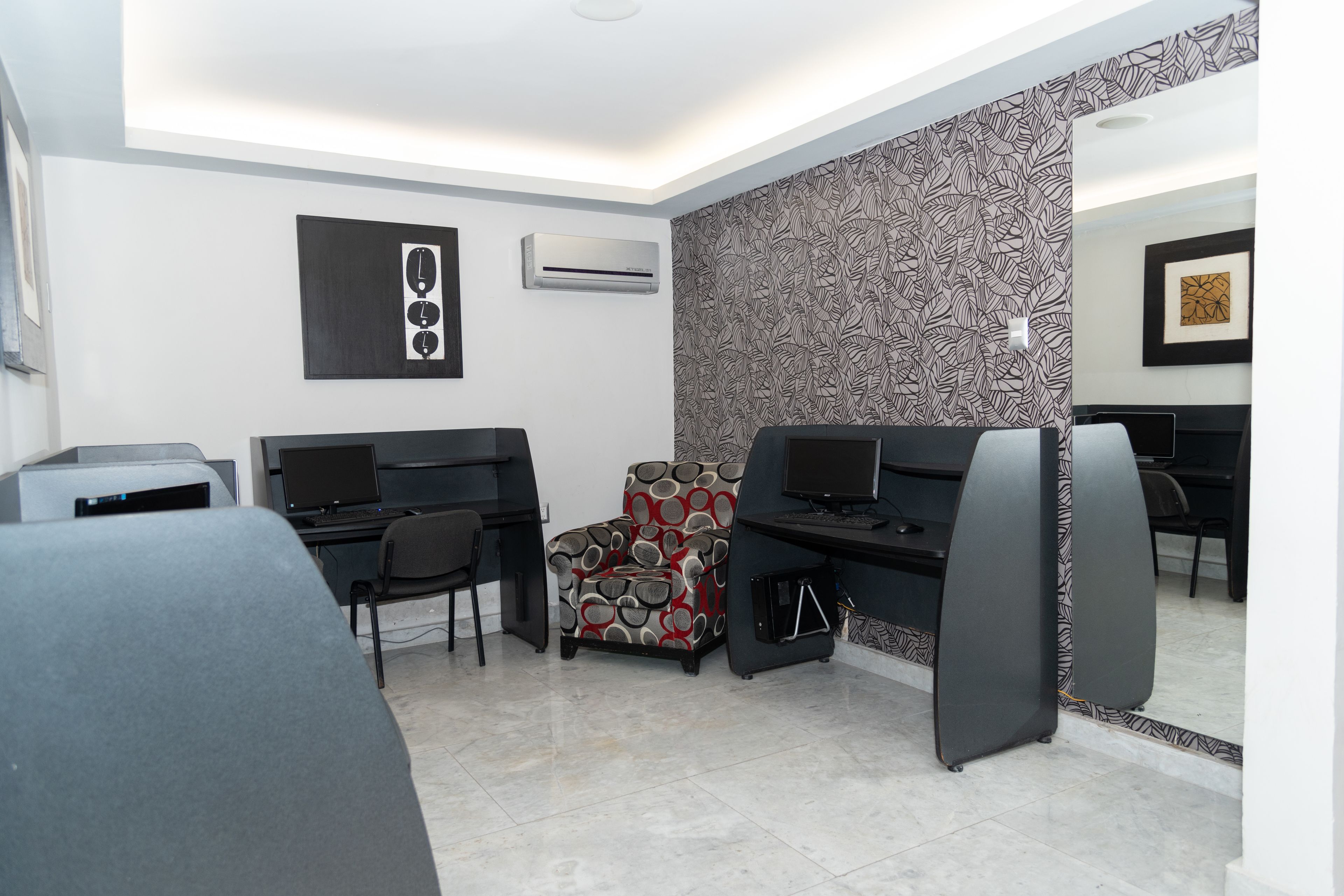 Un espacio de oficina moderno con dos escritorios, una silla estampada y un aire acondicionado de pared.