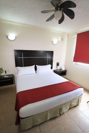 A neatly made bed with a red blanket, a black headboard, and a ceiling fan. - Hotel Estadio (Guadalajara)