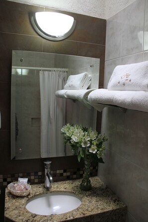 A bathroom with a sink, mirror, towel rack, and a vase with flowers. - Hotel Estadio (Guadalajara)