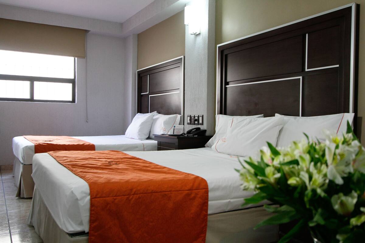 A hotel room with two single beds, a nightstand, a telephone, and a window.