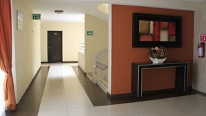 Un hall d’hôtel avec un escalier, un comptoir d’accueil et un extincteur fixé au mur.