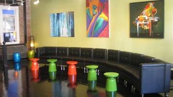 A modern lounge area with a curved black leather couch, colorful stools, and abstract paintings on the walls.