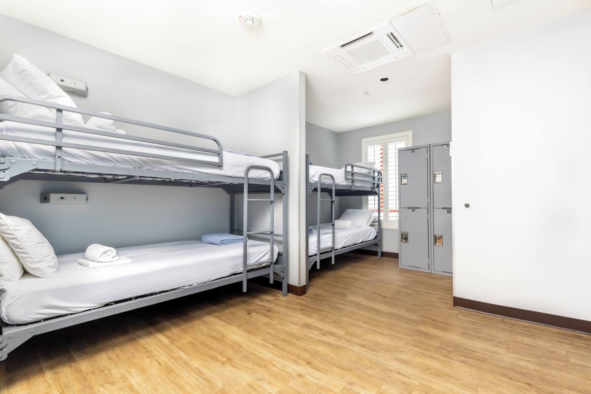 A dormitory room with bunk beds, a wooden floor, and a door leading to a bathroom.