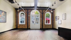 Una galería de arte con paredes de ladrillo, ventanas en arco y suelo de madera.