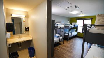 A hotel room with bunk beds, a sink, a mirror, and a window with a view.
