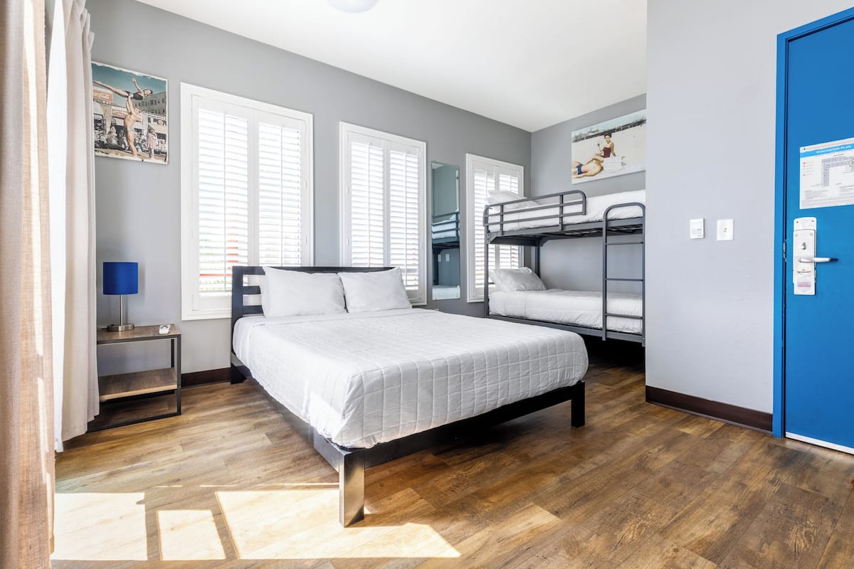 A bedroom with a large bed, a bunk bed, a desk, and a blue door.