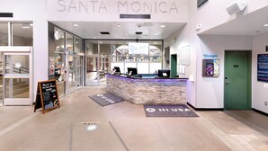 Un hall d'hôtel avec un comptoir d'accueil, une enseigne indiquant « SANTA MONICA » et une autre, accrochée au mur, portant la mention « Messages ».