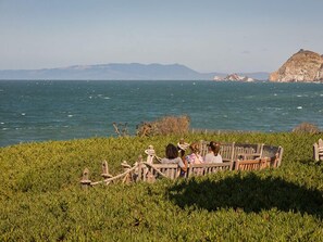 A wooden bench overlooking a body of water with a mountainous backdrop. - HI Point Montara Lighthouse Hostel (Moss Beach)