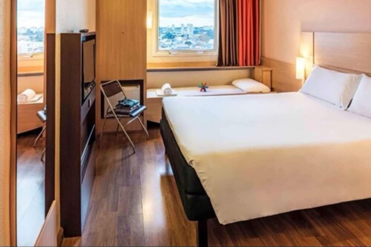 Une chambre d’hôtel comprenant un lit, un bureau, une chaise, une fenêtre donnant sur un paysage urbain et une armoire.