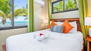 Une chambre d’hôtel avec un lit, des oreillers, une lampe et une vue sur les palmiers et la mer.