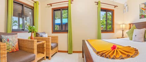 A hotel room with a bed, a sofa, a window with curtains, a painting on the wall, and a potted plant.