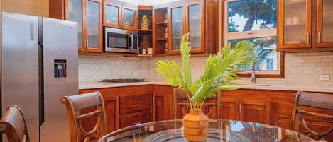 A kitchen with wooden cabinets, a stainless steel refrigerator, a microwave, and a glass dining table with chairs.