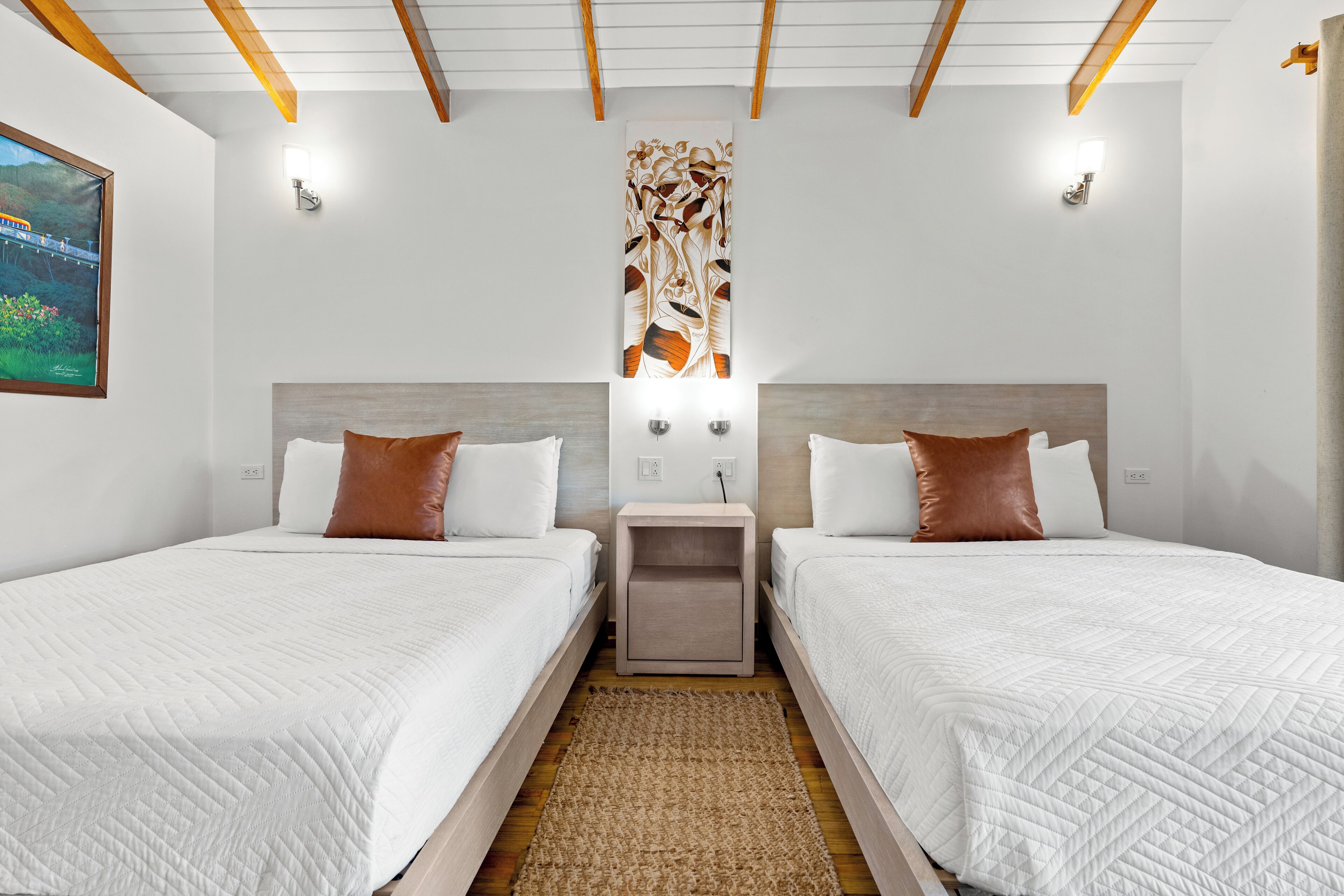 Ein Hotelzimmer mit zwei Betten, Holzboden, einem Wandbild und einem Nachttisch zwischen den Betten.