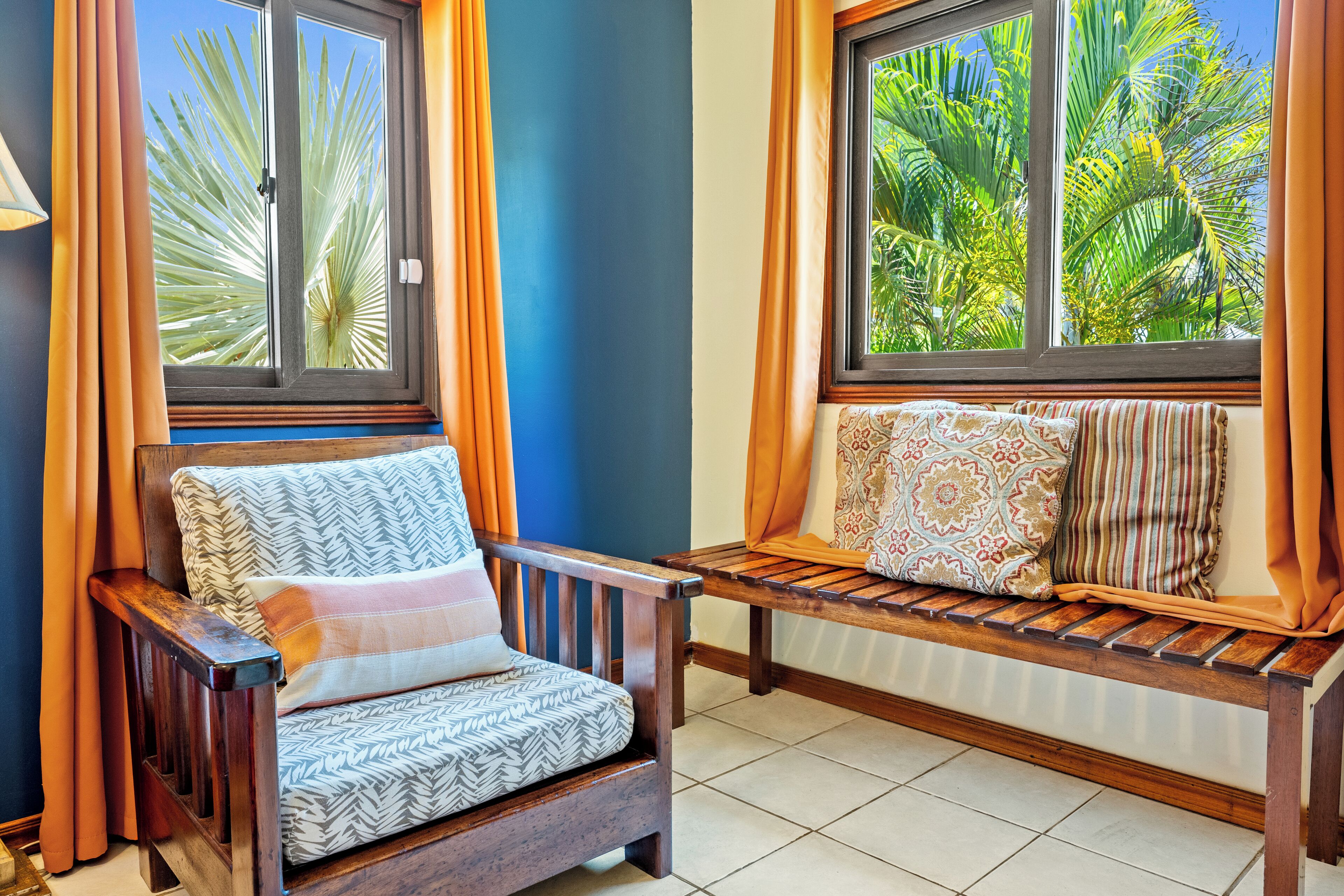 Una habitación con un banco de madera y un sillón con cojines estampados.