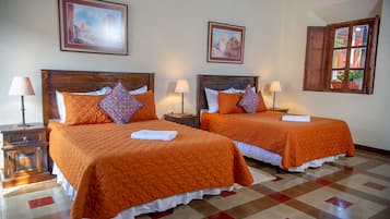 Hotelkamer met twee bedden, elk voorzien van een oranje sprei en bijpassende kussens, een houten hoofdbord, een nachtkastje met een lamp en een raam met uitzicht op gebouwen.