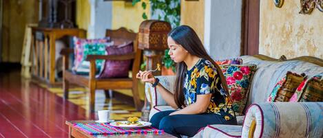 Una mujer sentada en un sofá frente a una mesa, con piso de madera y pared con diseño.