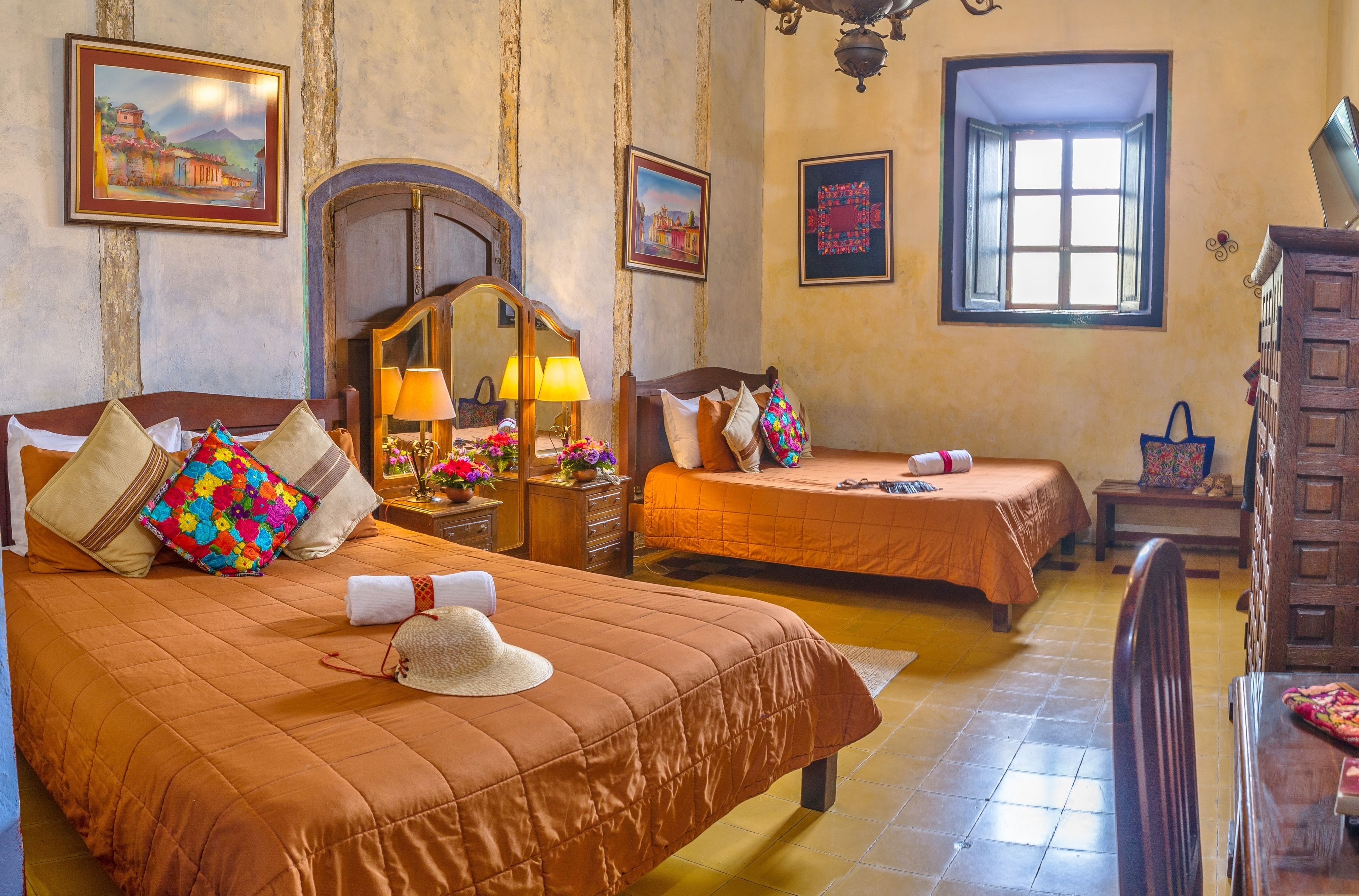 Quarto de hotel com duas camas, uma cômoda de madeira, um espelho e uma janela com vista.