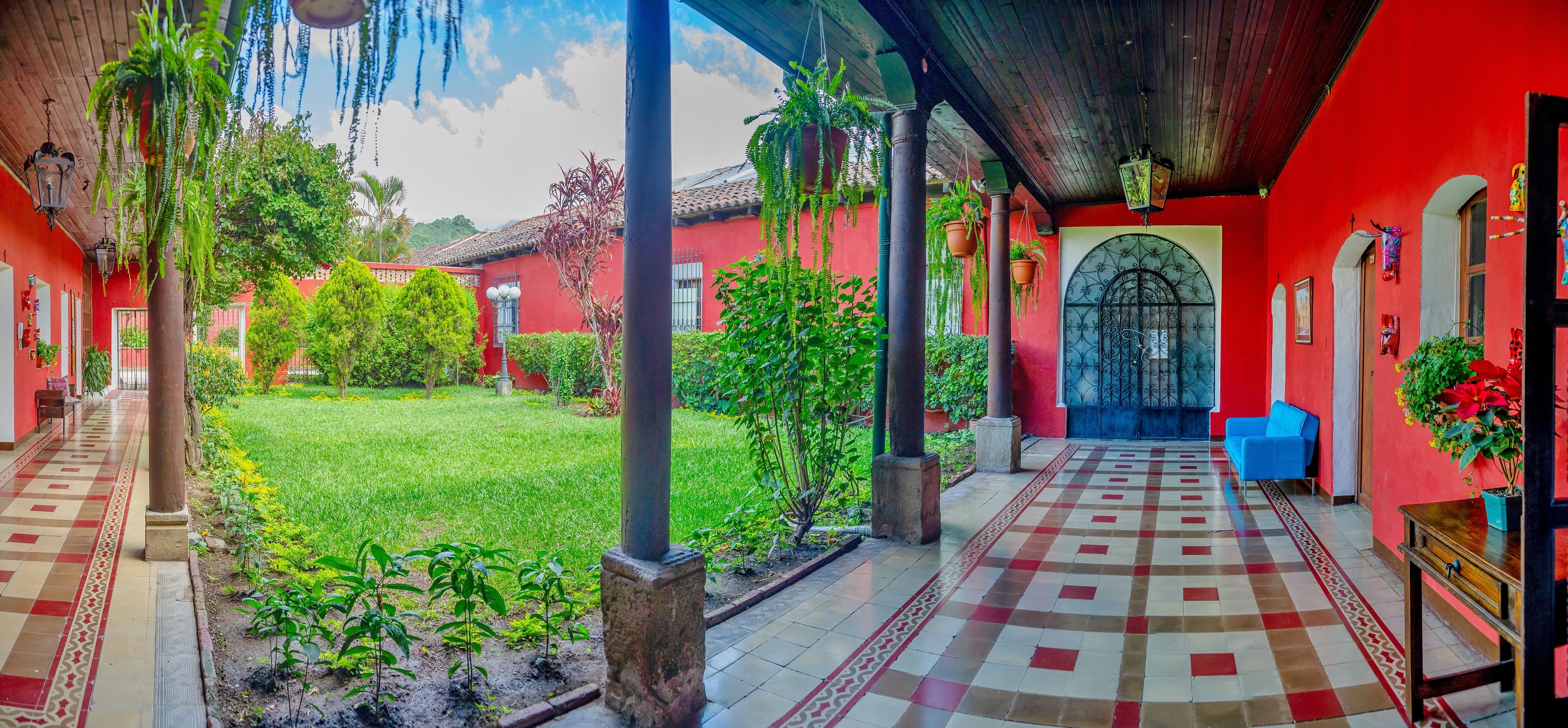 A covered outdoor area with a tiled floor, potted plants, and a red building with a blue door.