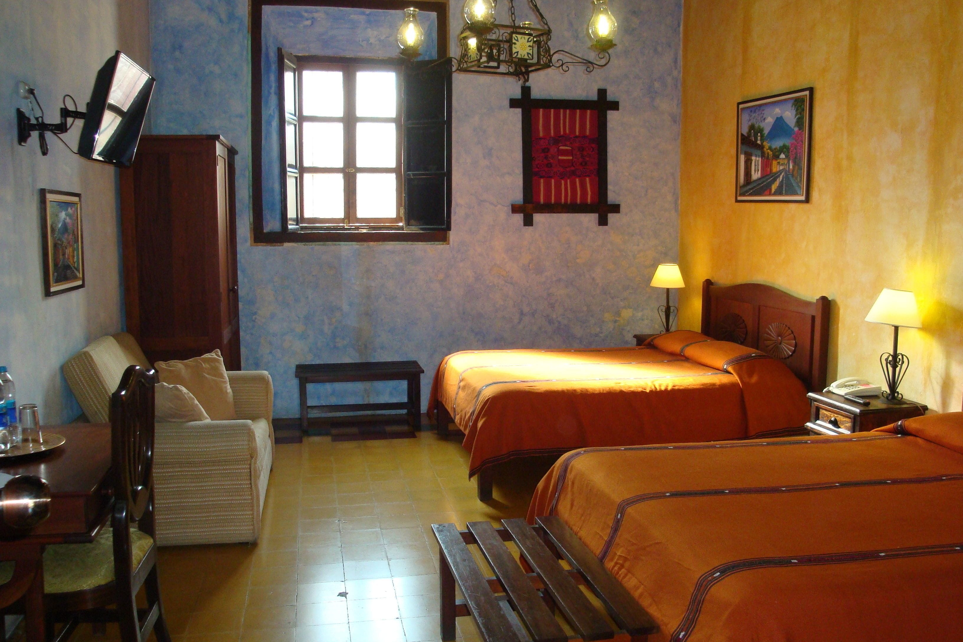 A hotel room with two beds, a dining table, a sofa, a wooden cabinet, a window with a view, and a painting on the wall.