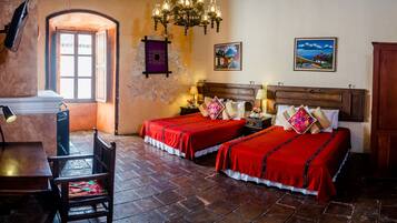 Una habitación de hotel con dos camas, un escritorio, una silla, una araña y obras de arte en las paredes.