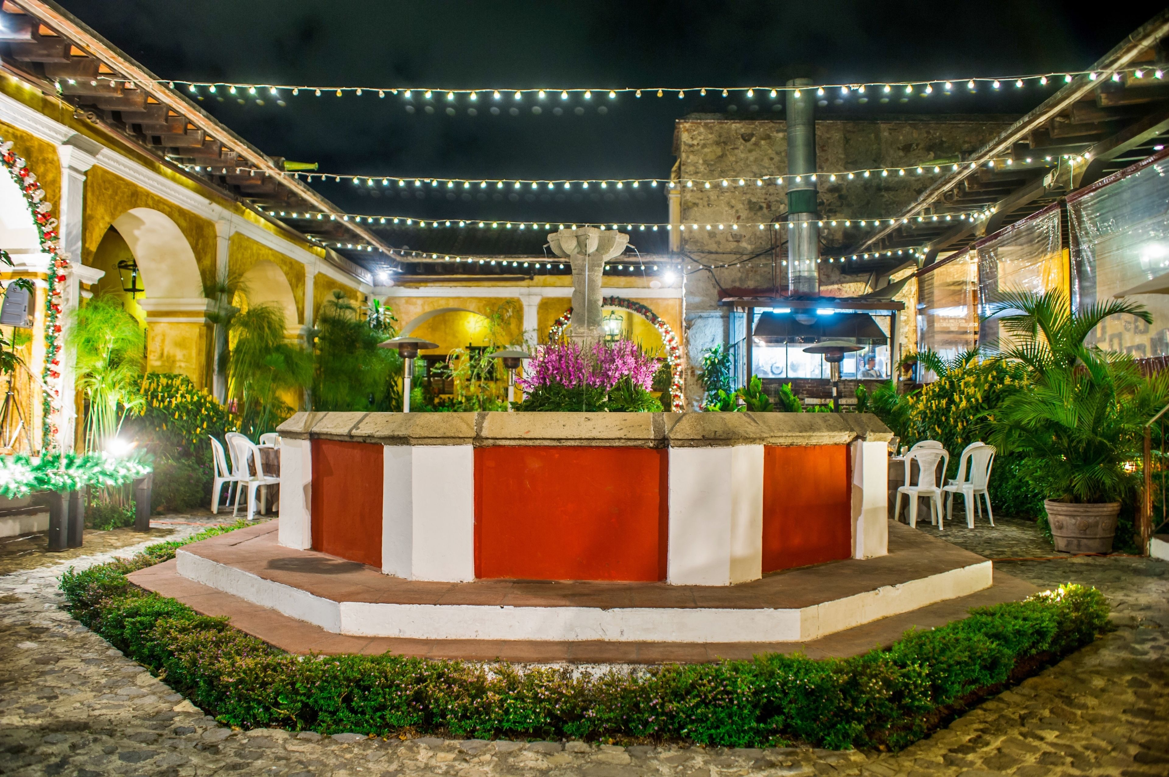 An outdoor courtyard with a central seating area, surrounded by greenery and potted plants.