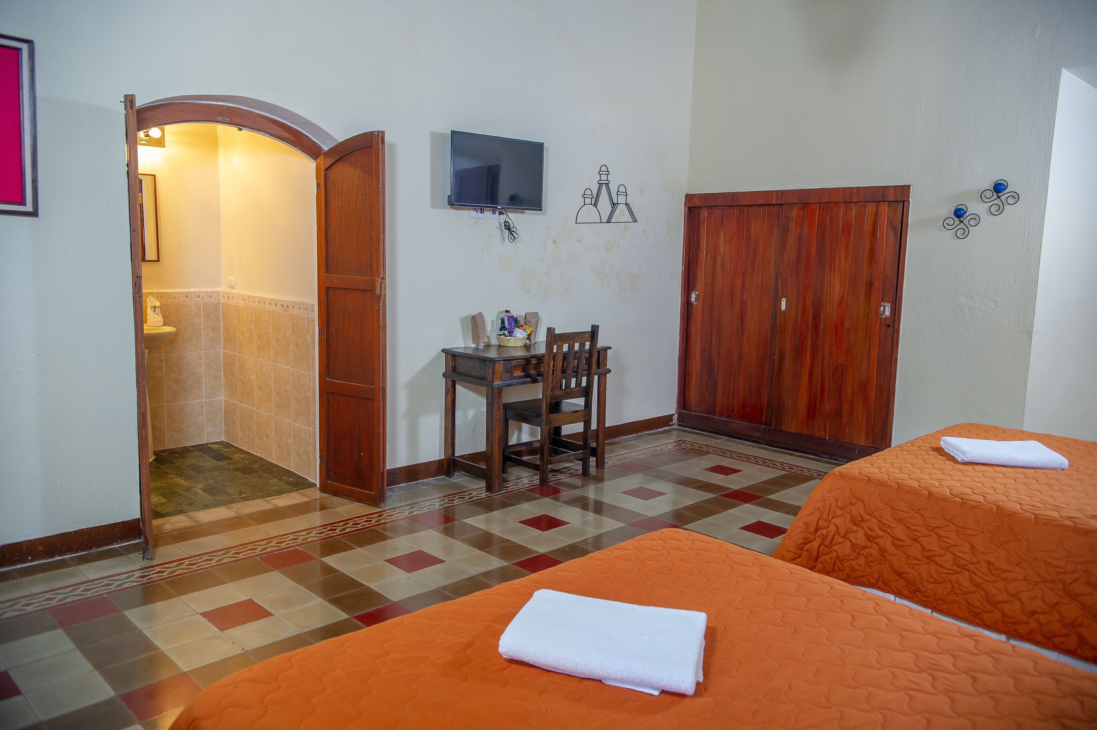 A hotel room with two beds, a desk, a television, and a shower area.