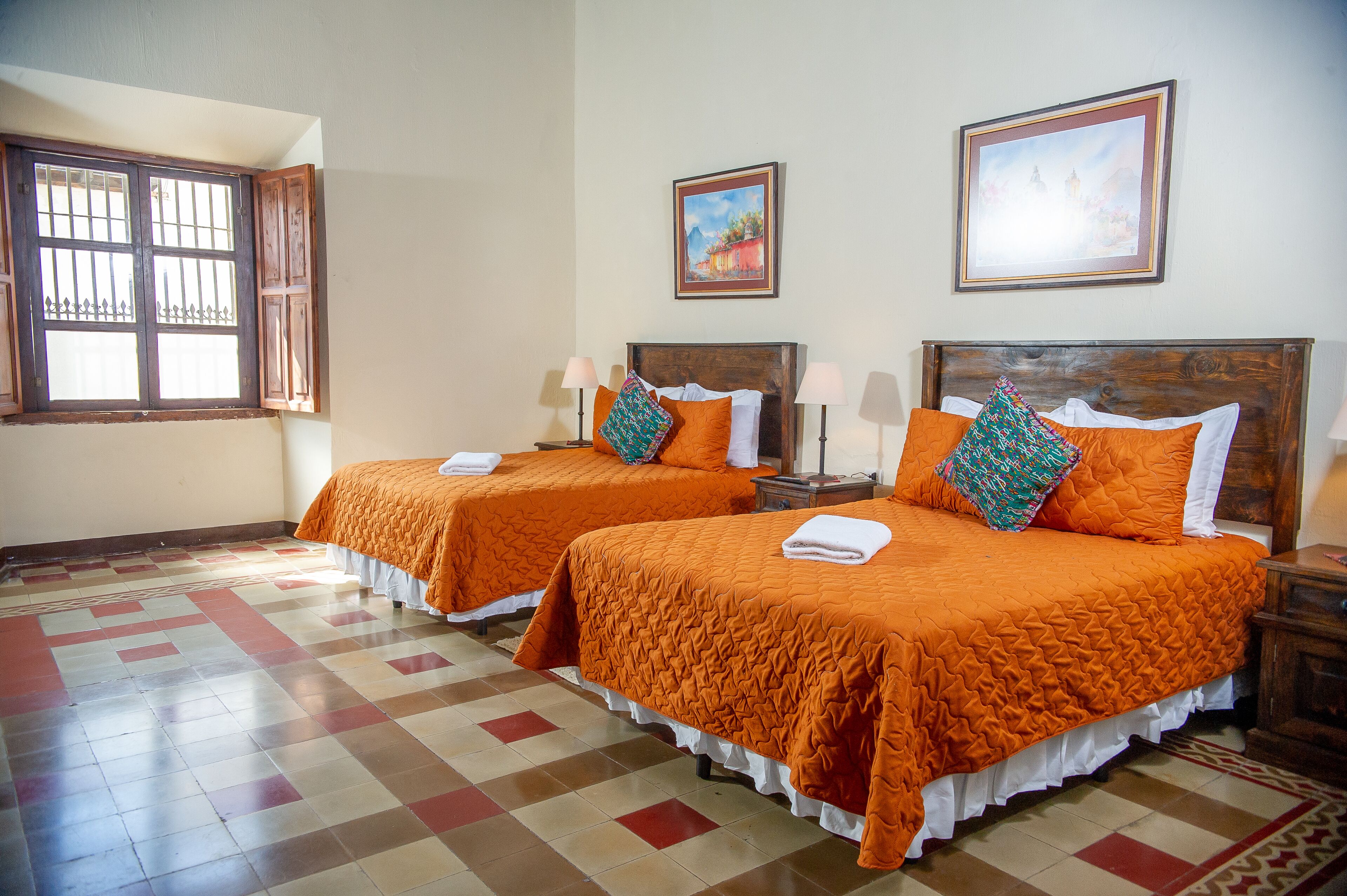 A hotel room with two beds, a window with bars, and two paintings on the wall.