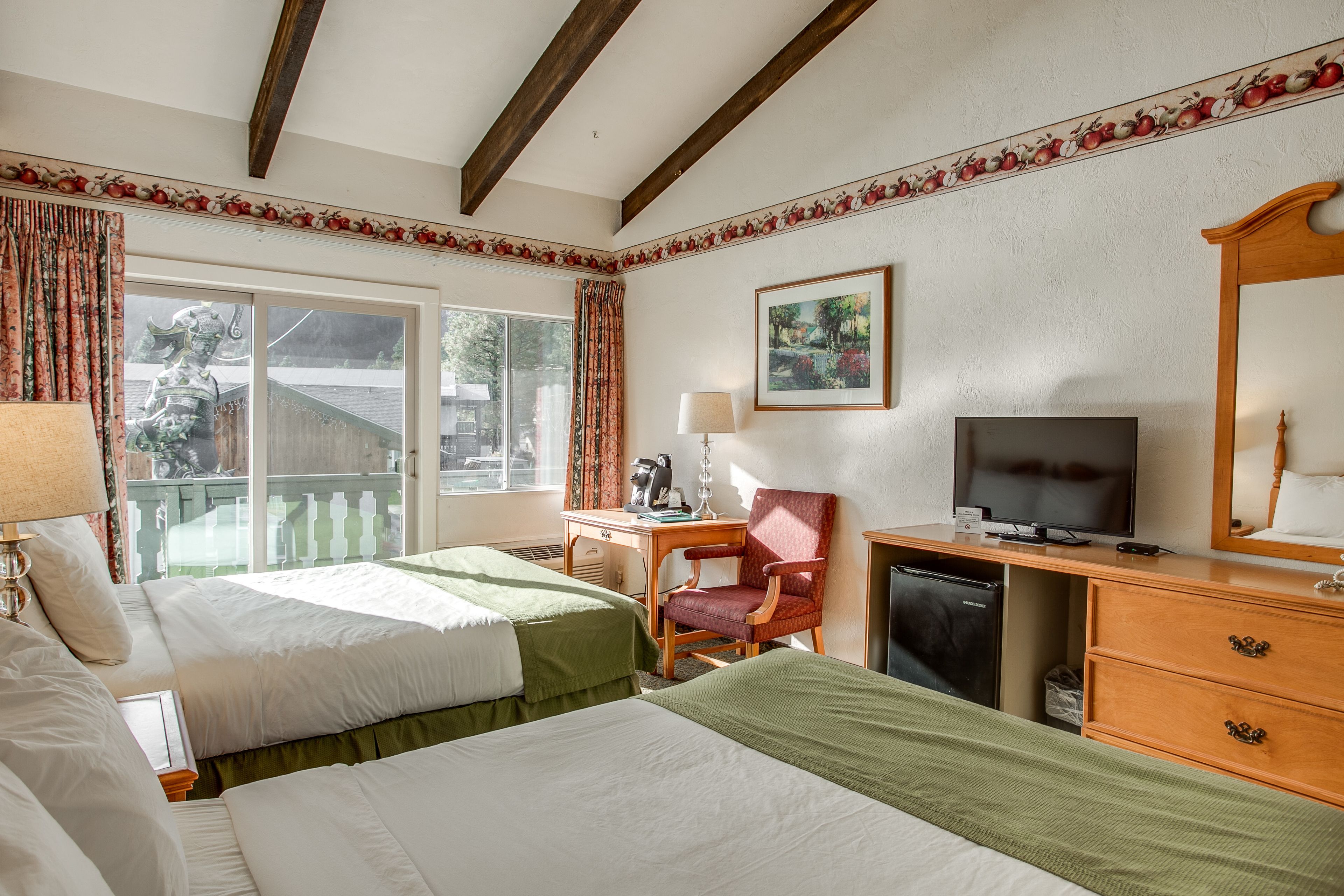 A hotel room with two beds, a desk with a television, a chair, and a small refrigerator.