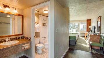 A bathroom with a sink, toilet, and shower. There is a mirror above the sink and a window in the adjacent room.