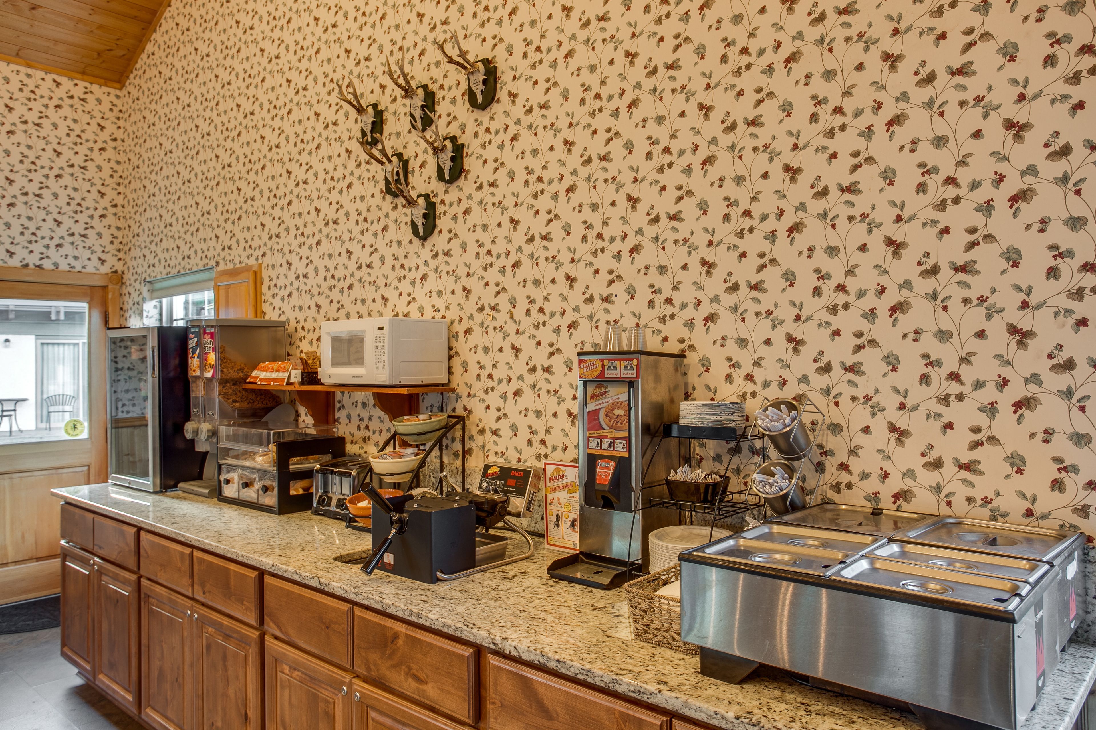 A kitchen with wooden cabinets, a granite countertop, a coffee machine, a microwave, and a refrigerator.