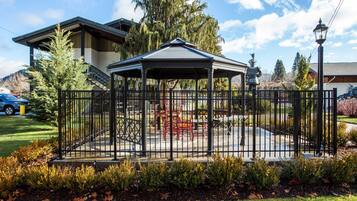 A gazebo with a metal fence, surrounded by a garden with shrubs and a lawn.