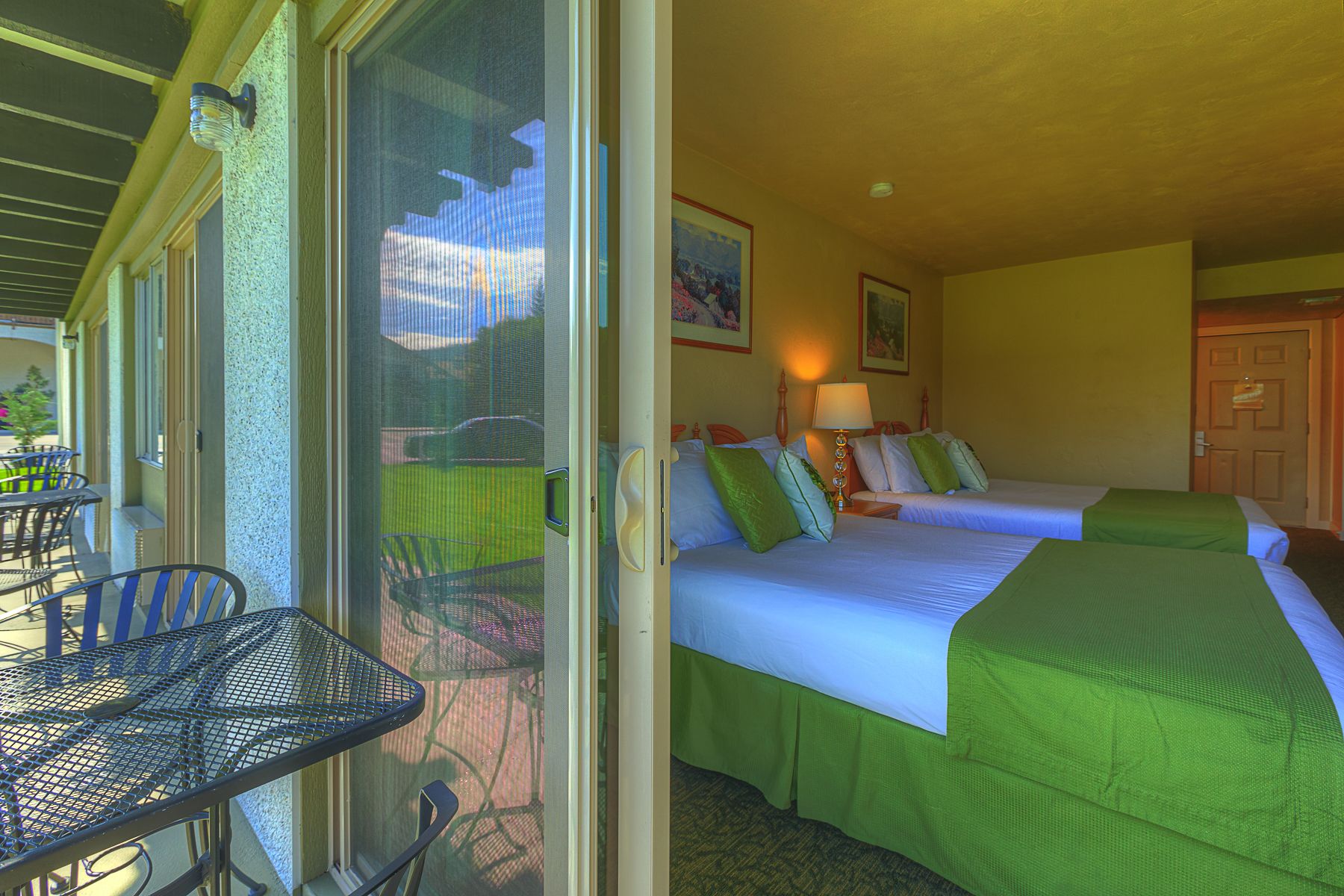 Une chambre d’hôtel avec deux lits, un balcon doté d’une table et de chaises, et une vue sur l’extérieur.