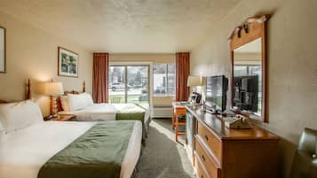 Quarto de hotel com duas camas, uma mesa de trabalho com televisão, cômoda e uma janela grande com cortinas.