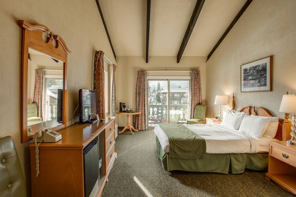 A hotel room with a bed, a desk, a telephone, and a window with curtains.