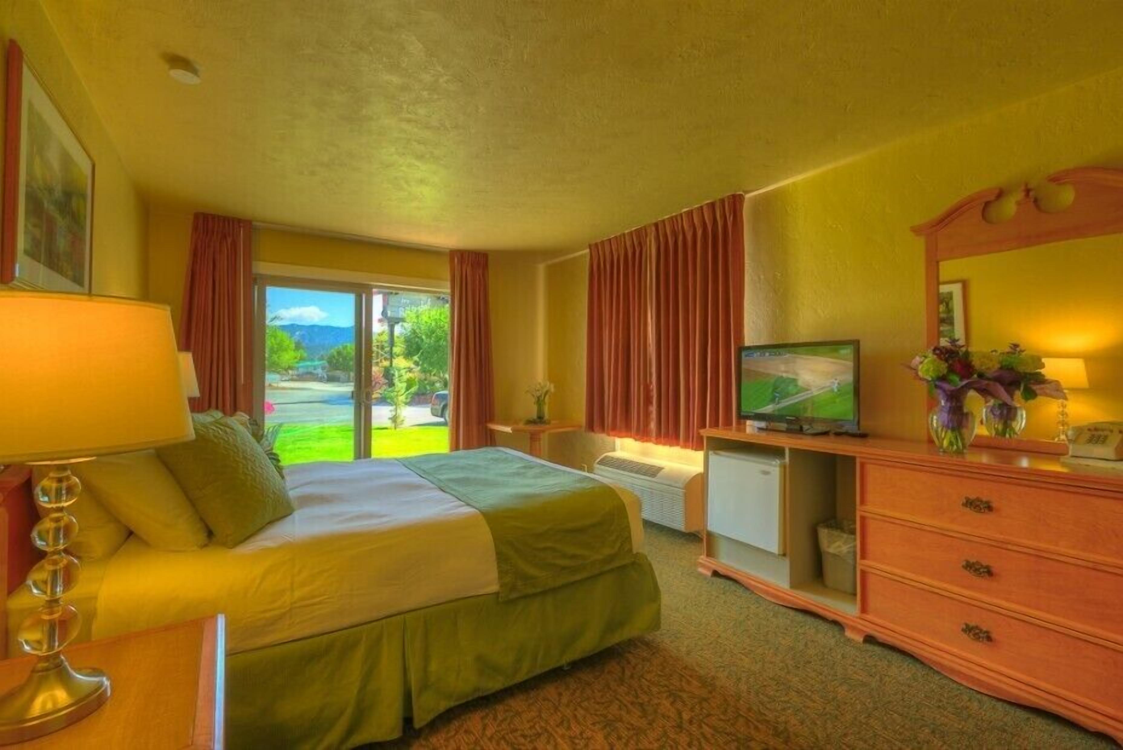 A hotel room with a bed, a television, a desk, and a dresser.